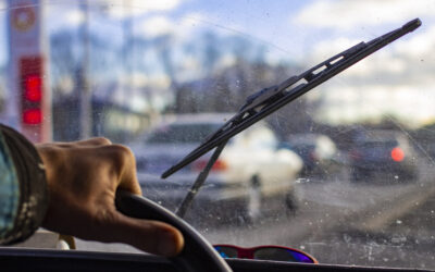 Person is driving a car with windshield covered with scratches and dirt. View from inside the car.
